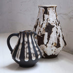 Two ceramic pitchers with black and white abstract patterns on a light surface.