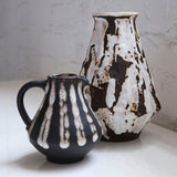 Two ceramic pitchers with black and white abstract patterns on a light surface.