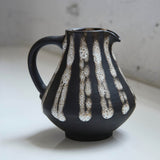 Black ceramic pitcher with white abstract patterns on a light background