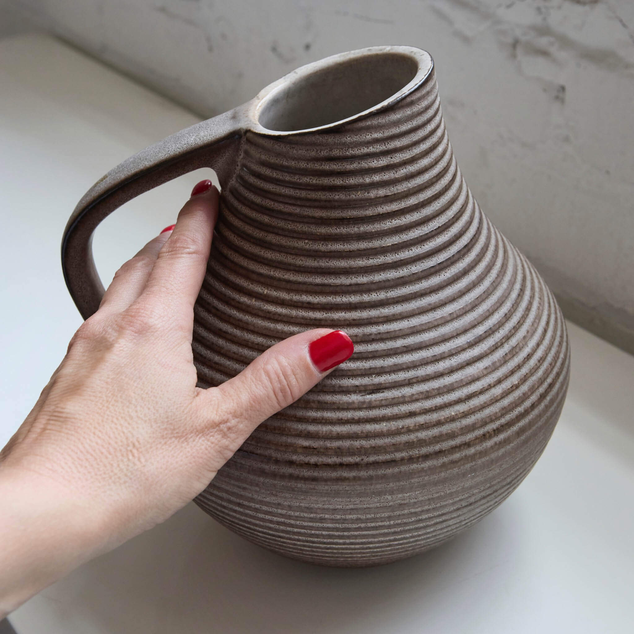 Hand holding a textured stoneware pitcher against a neutral background