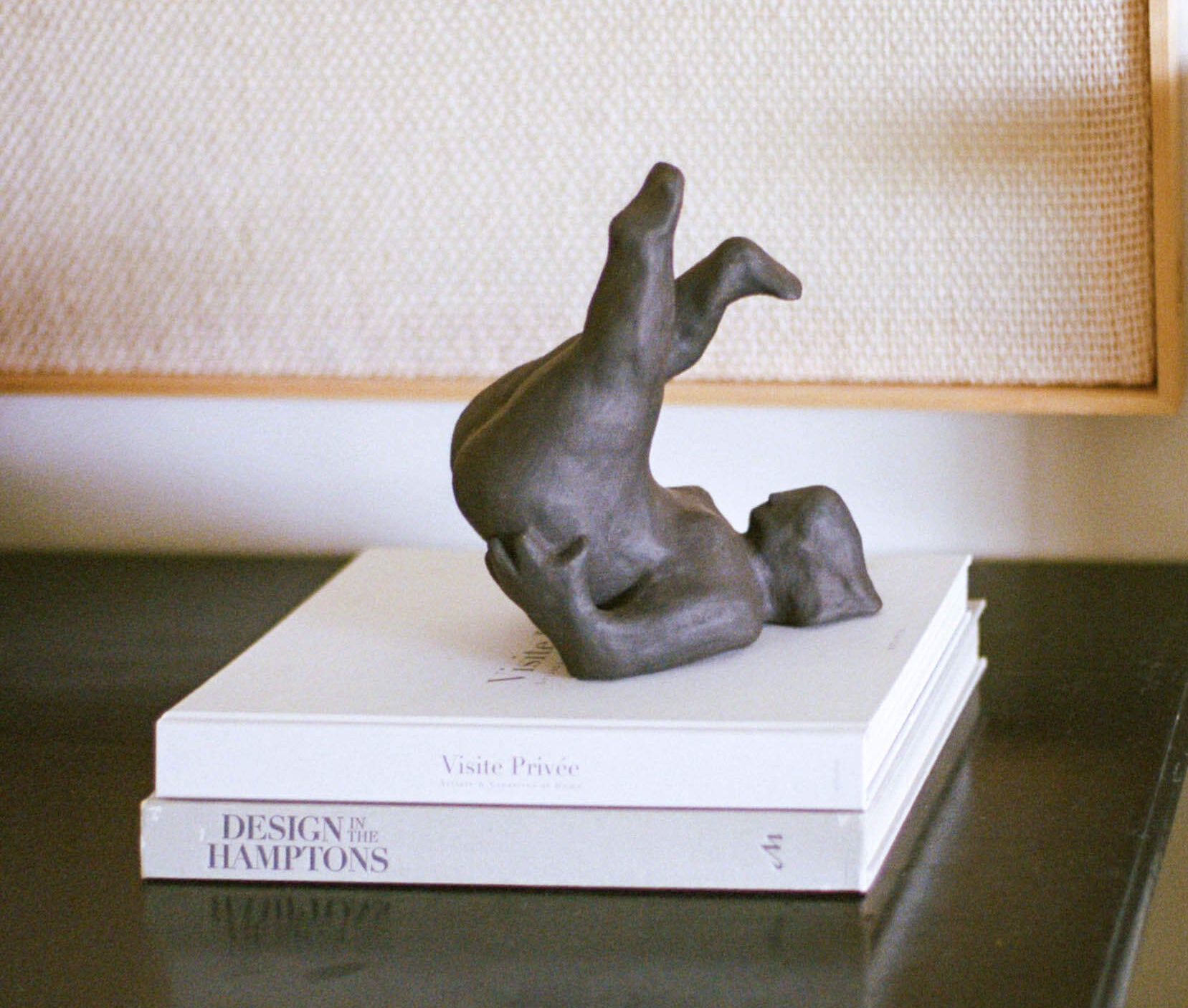 Black sculpture on top of books on a dark wooden table with a lamp in the background